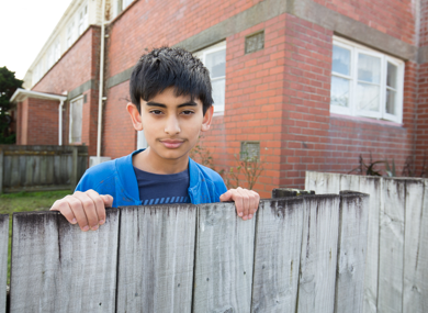 Boy looks over fence outside brick house
